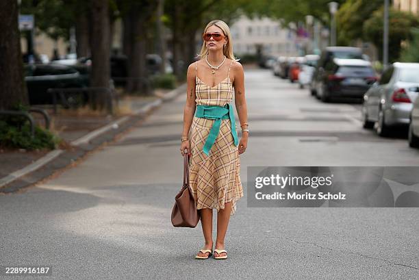 Julia Kammerer is seen wearing a beige plaid midi dress from Mango; a wide turquoise fabric belt from Mango; beige flip flops from Ulanka; a large...
