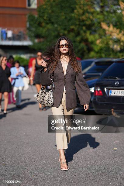 Guest wears long wavy brown hair with a center part, brown rectangular sunglasses with tinted lenses, a brown check oversized blazer jacket with a...