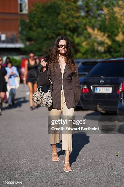 Guest wears long wavy brown hair with a center part, brown rectangular sunglasses with tinted lenses, a brown check oversized blazer jacket with a...