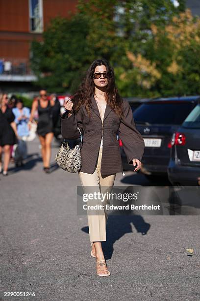 Guest wears long wavy brown hair with a center part, brown rectangular sunglasses with tinted lenses, a brown check oversized blazer jacket with a...
