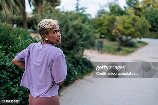 athletic woman looking back over shoulder in park - running looking back stock pictures, royalty-free photos & images