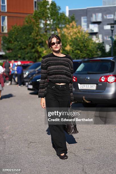 Guest wears dark brown hair in a center-part bun, brown rectangular sunglasses with tinted lenses, a black and gray striped knit cropped sweater,...