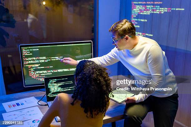 two computer programmers are collaborating closely on a software development project. pointing at intricate code displayed on a computer monitor and using a tablet - devops stock pictures, royalty-free photos & images