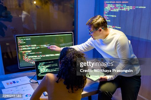 Two computer programmers are collaborating closely on a software development project. Pointing at intricate code displayed on a computer monitor and using a tablet Two computer programmers are collaborating closely on a software development project. Pointing at intricate code displayed on a computer monitor and using a tablet