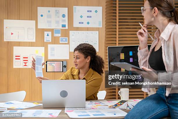 ux/ui designers discussing and brainstorming on wireframes for a website and mobile app prototype, surrounded by sketches of user flow and design tools, in the concept of website and mobile application design concept. - website wireframes stock pictures, royalty-free photos & images