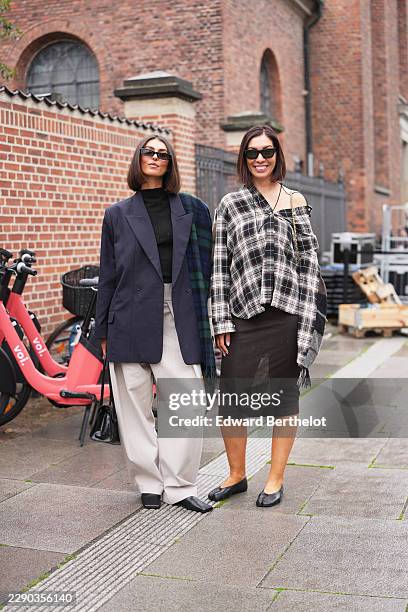 Guest wears dark brown bob hair with a center part, black rectangular sunglasses, a navy oversized blazer jacket, a blue and green plaid scarf, a...