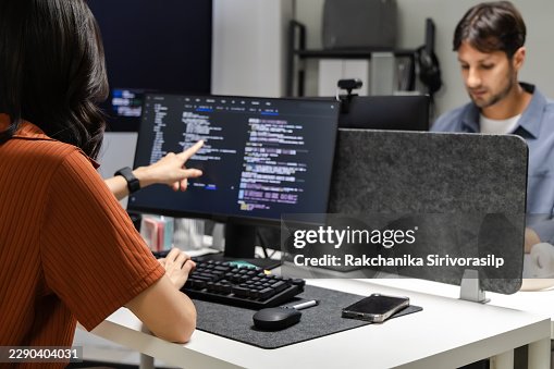 Software developer pointing at source code on monitor during office code review, analyzing programming logic and debugging details to improve software development quality. Software developer pointing at source code on monitor during office code review, analyzing programming logic and debugging details to improve software development quality.