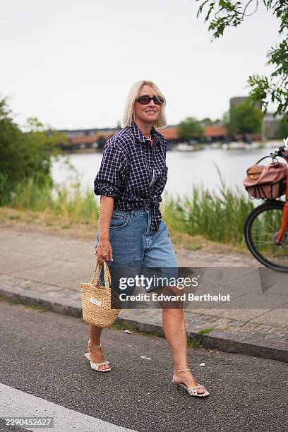 Guest wears shoulder-length straight blonde bobbed hair, black oval Miu Miu sunglasses with dark lenses, a navy and white plaid long-sleeve...