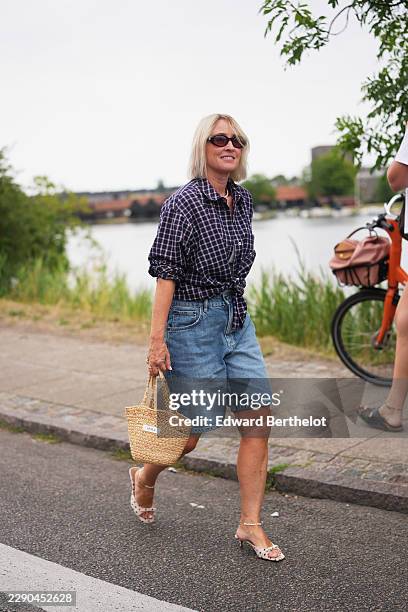 Guest wears shoulder-length straight blonde bobbed hair, black oval Miu Miu sunglasses with dark lenses, a navy and white plaid long-sleeve...