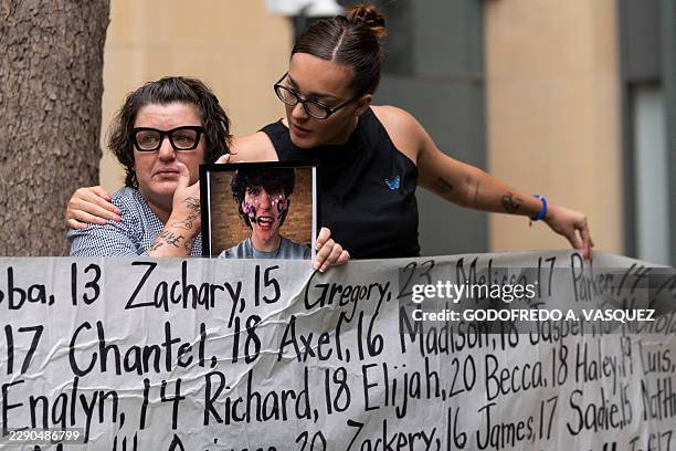 Shannon Heacock is comforted by Lennon Torres while Heacock holds a photograph of her son and a banner with the names of nearly 400 of young people...
