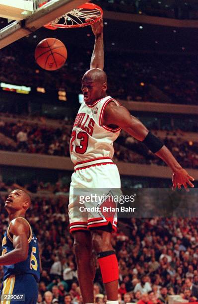 Guard Michael Jordan of the Chicago Bulls slam dunks Golden State Warriors guard Latrell Sprewell watches during their game at the United Center in...