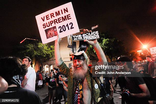 View of American performance artist Vermin Supreme, holding a sign and a bumper sticker, during an 'Occupy Southby' march , on East Sixth Street,...