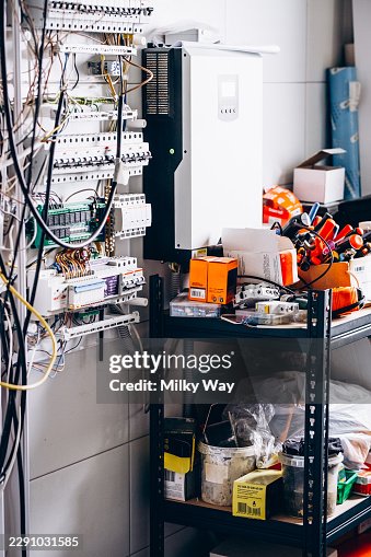 Electrical switchboard with circuit breakers, wiring, and wall-mounted inverter in a utility room under installation. Electrical switchboard with circuit breakers, wiring, and wall-mounted inverter in a utility room under installation.