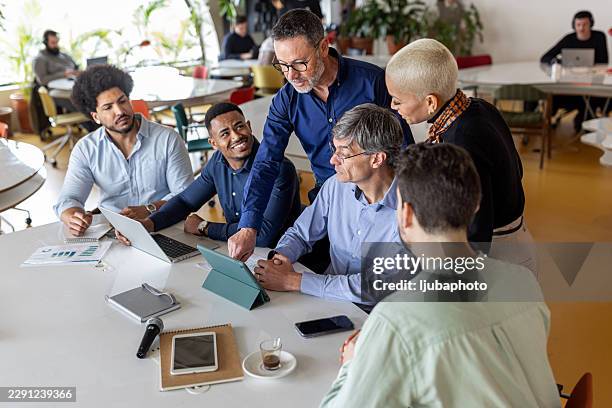 multigenerational team meeting in modern coworking office with leader mentoring colleagues around tablet - generation gap stock pictures, royalty-free photos & images