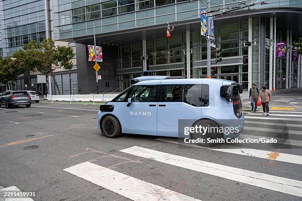 Waymo Ojai autonomous robotaxi travels through the Fourth and Howard streets intersection outside Moscone West, which displays banners for the 2026...