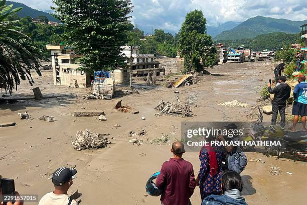 Residents look at houses partially submerged in muddy water after flash floods at Trishuli Bazar in Nepal's Nuwakot district on August 26, 2026. A...
