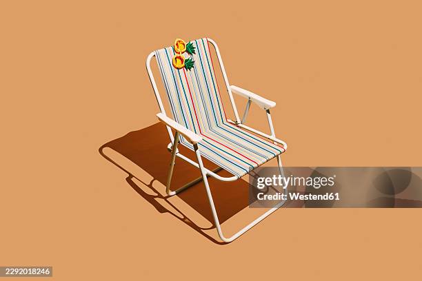 pineapple eyewear rests on an empty striped beach chair - light peach background stock illustrations