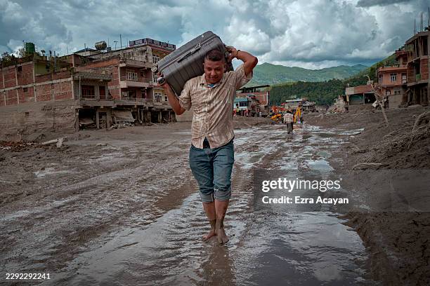 Resident carries belongings across a road heavily covered in mud following flash floods on August 27, 2026 in Trishuli, Nepal. A sudden flood swept...