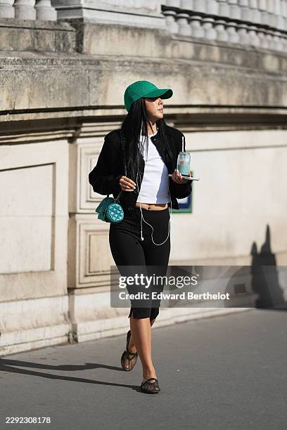 Yuwei Zhangzou wears a green baseball cap hat by Ralph Lauren, white wired earphones, uses an Apple iPhone, drinks a green drink of matcha latte...