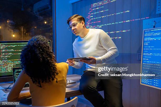 young latin software developers team meeting discussing source code on desktop monitor working late in dark office at night. artificial intelligence and programming concept. - api developer stock pictures, royalty-free photos & images