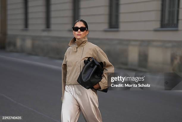 Aylin Sengül is seen wearing a beige cropped trench coat from COS; cream satin wide leg trousers from Almada Label; a large black leather tote Trullo...
