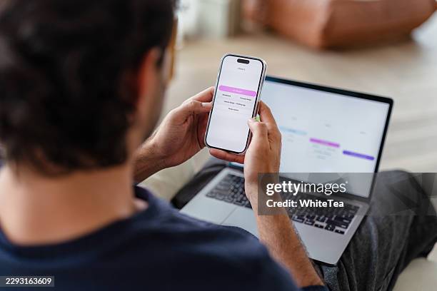 man managing schedule on smartphone while using laptop - gantt chart stock pictures, royalty-free photos & images