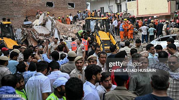 People gather to watch as rescue personnel conduct a search operation at the site following a building collapse in the Satya Niketan area in New...