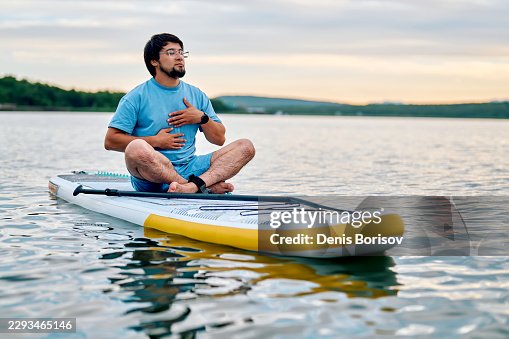 Man practicing breathing exercise and mindfulness while sitting on paddleboard Man practicing breathing exercise and mindfulness while sitting on paddleboard