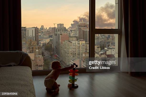 Nine-month-old Noi, son of Ukrainian photographers Kostiantyn Liberov and Vlada Liberova, plays by a window as smoke rises outside following a...