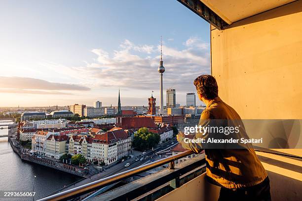 traveler looking at berlin skyline and fernsehturm from balcony at sunset, germany - berliner fernsehturm stock-fotos und bilder