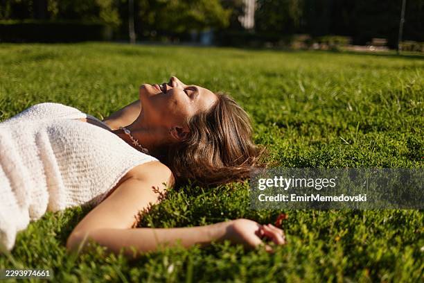 young woman relaxing lying on green grass enjoying sunshine - composition stock pictures, royalty-free photos & images