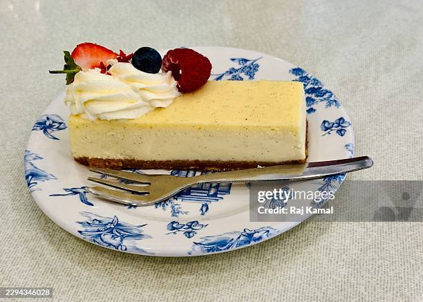 vanilla cheescake with digestive biscuit base, fresh cream decoration on top with raspberry, strawberry and blueberries on a plate with fork. - digestive biscuit stock pictures, royalty-free photos & images