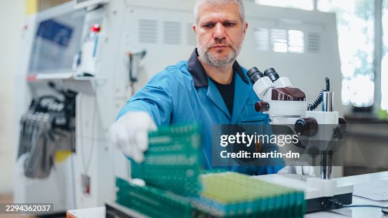 Electronics Engineer Inspecting Printed Circuit Board Under Microscope During Quality Control Electronics Engineer Inspecting Printed Circuit Board Under Microscope During Quality Control