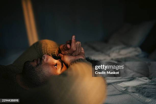 thoughtful man lying down on bed at home - clothes on bed stock pictures, royalty-free photos & images