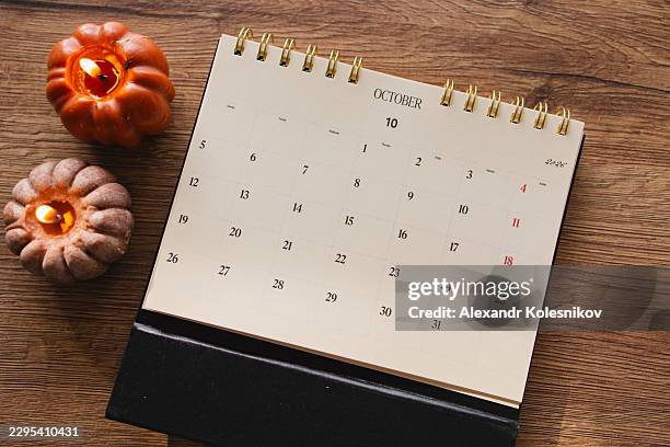 october calendar decorated with pumpkin-shaped candles on a wooden table, illustrating autumn planning, seasonal organization and preparation. cozy fall still life with copy space. - outubro imagens e fotografias de stock