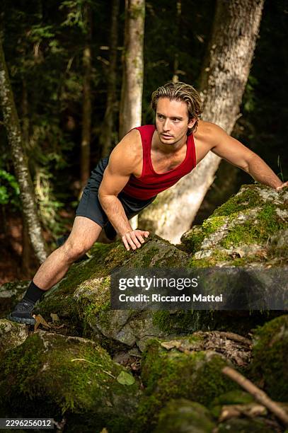 young man climbing over rocks during primal fitness workout in forest - fixed mindset stock pictures, royalty-free photos & images