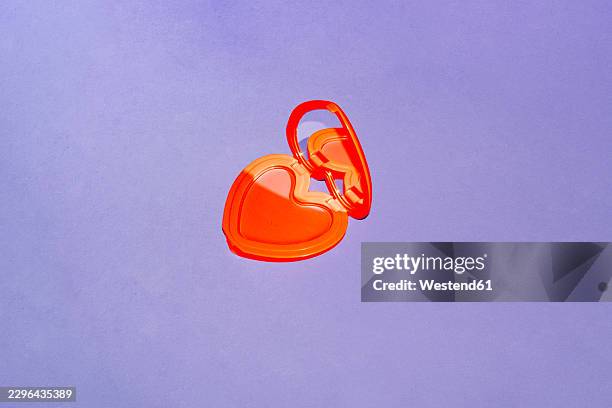 a red heart makeup compact rests on a purple background - red plastic background stock illustrations