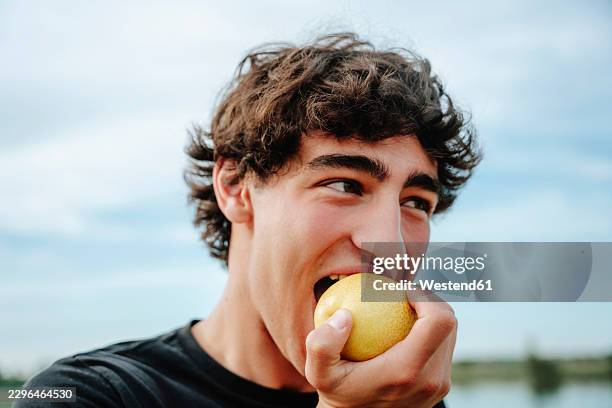 young man eats a fresh apple outside - man biting apple stock pictures, royalty-free photos & images
