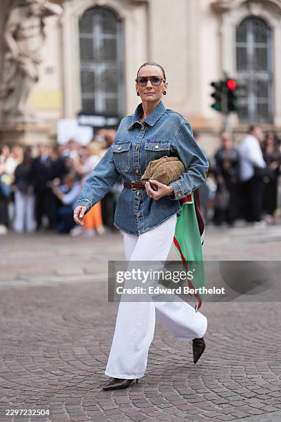 Guest wears slicked back dark brown hair, brown aviator sunglasses with tinted lenses, black and red logo pattern earrings from Chanel, a blue denim...