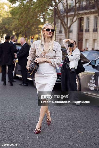 Leonie Hanne wears a pale beige button up shirt with a matching knee length pencil skirt, black sunglasses, a black leather handbag, and burgundy...