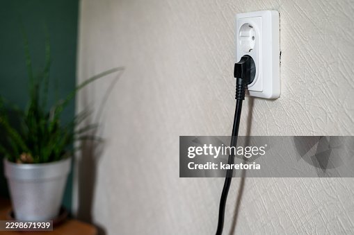 White plastic wall socket with black plug and cable inserted White plastic wall socket with black plug and cable inserted