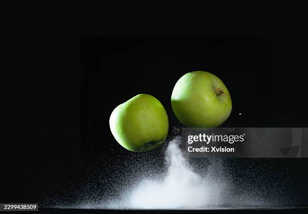 green apple flying in mid air with flour exploding in black background - exploding apple stock pictures, royalty-free photos & images