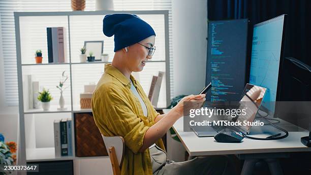 young asian female software engineer with cancer patient using smartphone while coding on computer in home office. network security, chatbot, software development, artificial intelligence concept. - javascript stock pictures, royalty-free photos & images
