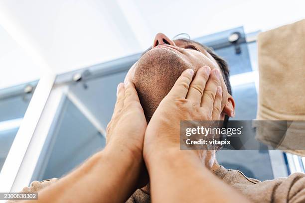 man applying aftershave in bathroom mirror during morning grooming routine - aftershave stock pictures, royalty-free photos & images