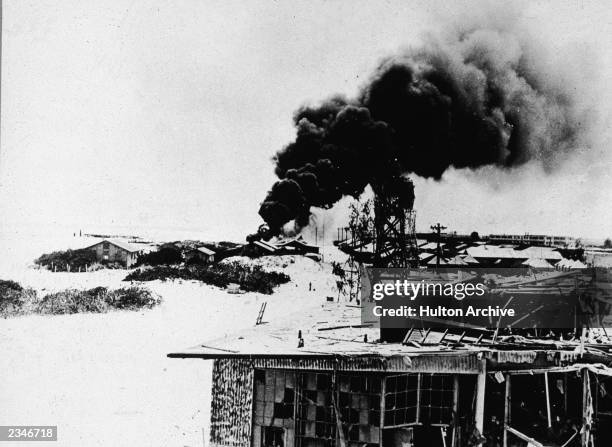 Black smoke pours from demolished buildings after Japanese air forces attacked the US Navy base on Midway Atoll the Battle of Midway, World War II,...
