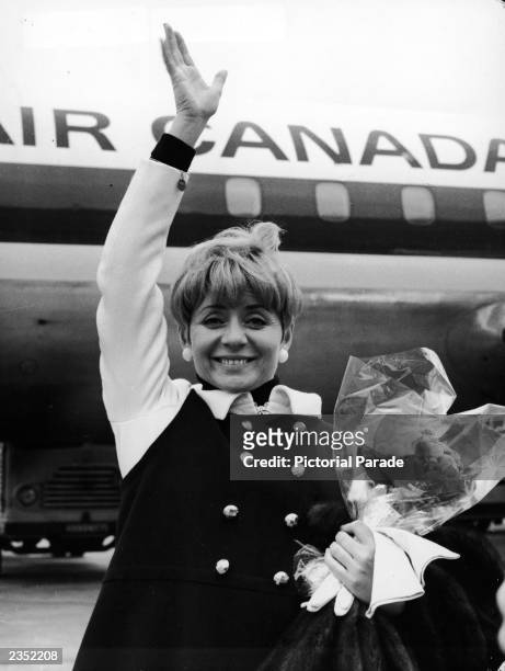 French singer Annie Cordy waves while holding a bouquet of flowers at Orly Airport, Paris, France, April 4, 1967. Cordy was en route to Montreal to...