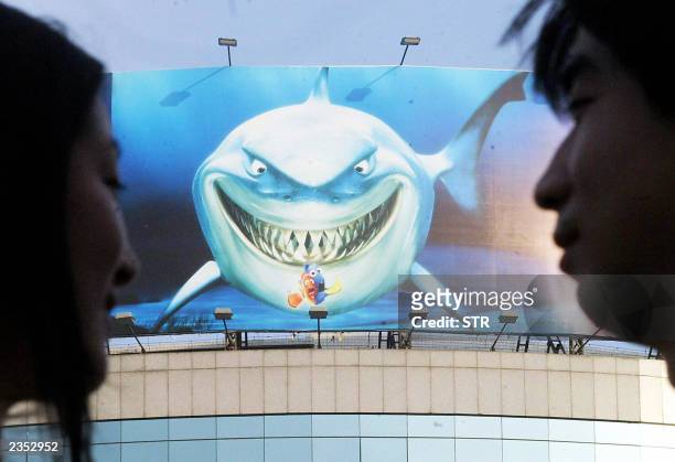 Chinese couple prepare to visit a new aquarium displaying a poster of hollywood film "Finding Nemo", in Beijing 29 July 2003. Tourism and travel to...