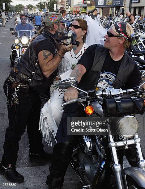 Newlywed bride gets a kiss from a man on the street as her husband looks on in Sturgis, South Dakota during the annual Sturgis Motorcycle Rally...