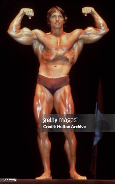 Austrian born actor and former bodybuilder Arnold Schwarzenegger poses in a bathing suit and flexes his muscles in a bodybuilding pose, circa 1980....