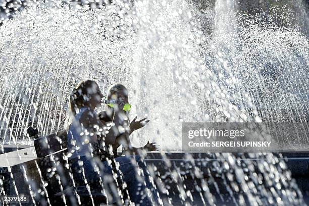 Girl drinks lemonade with her girlfriend as they refresh themselves by fountains in Kiev 04 August 2003.